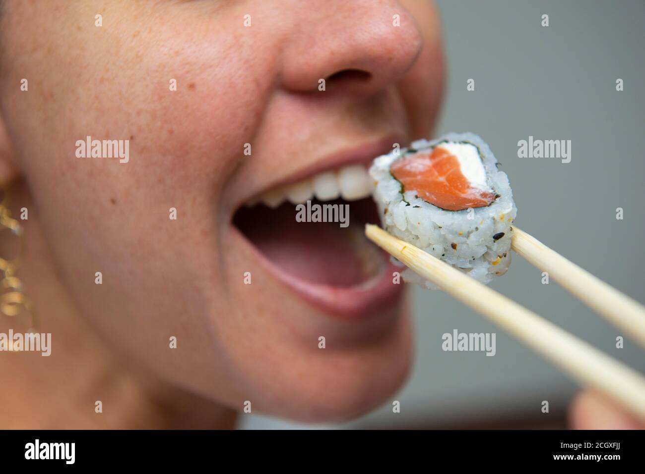 Nahaufnahme des Frauenmundes beim Essen von köstlichem Lachs-Sushi (Uramaki). Japanische Küche. Selektiver Fokus. Japanische Küche. Stockfoto