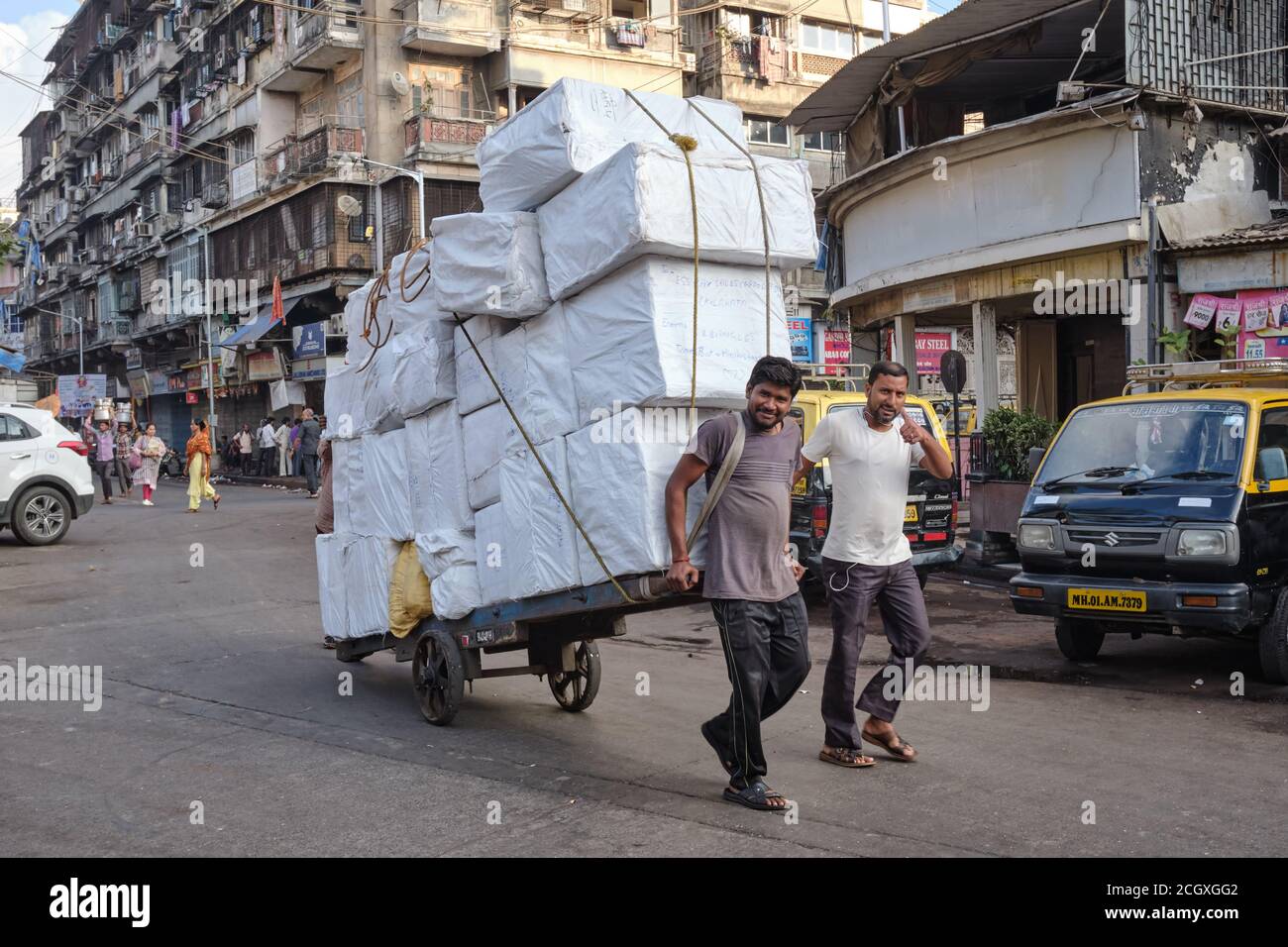 Fröhliche Handkarrenabzieher in Mumbai, Indien, ziehen einen Wagen mit fast einer Tonne Ballen Stoff geladen Stockfoto