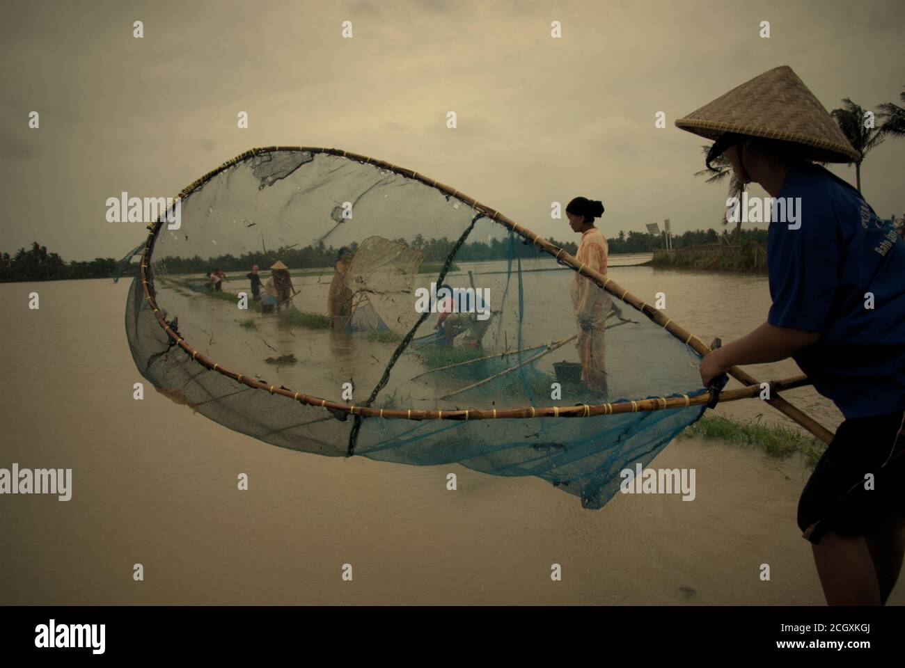 Menschen, die während einer Regenzeit auf einem überschwemmten Reisfeld mit Schleppnetzen fischen, die Überschwemmungen in Karawang Regency, Provinz West Java, Indonesien verursachen. Stockfoto