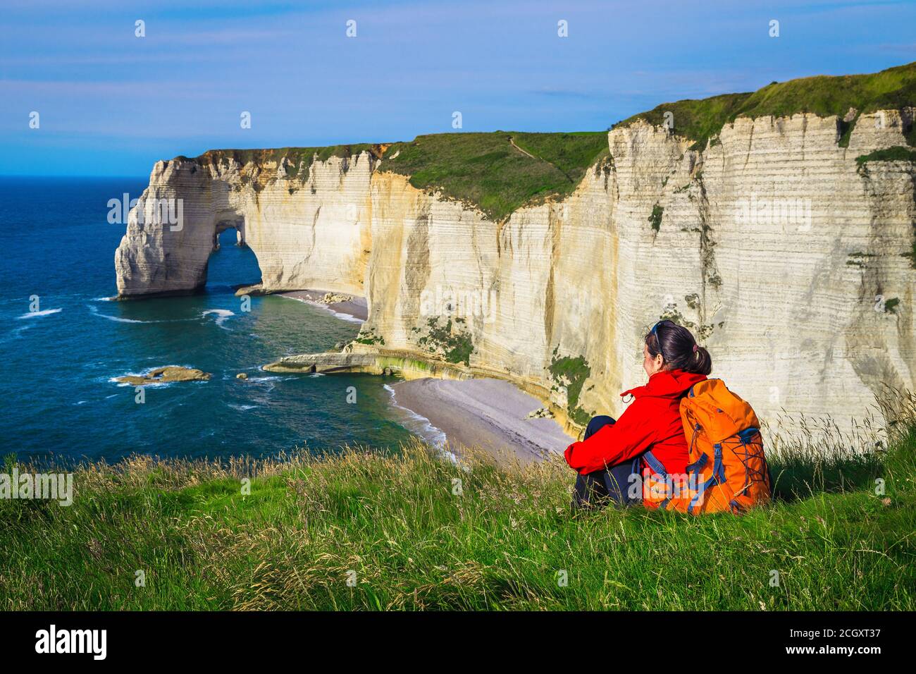 Sorglose glückliche Reisende Frau entspannend und genießen Sie die Aussicht mit Meer. Backpacker Frau sitzt im grünen Gras, Etretat, Normandie, Frankreich, Europa Stockfoto