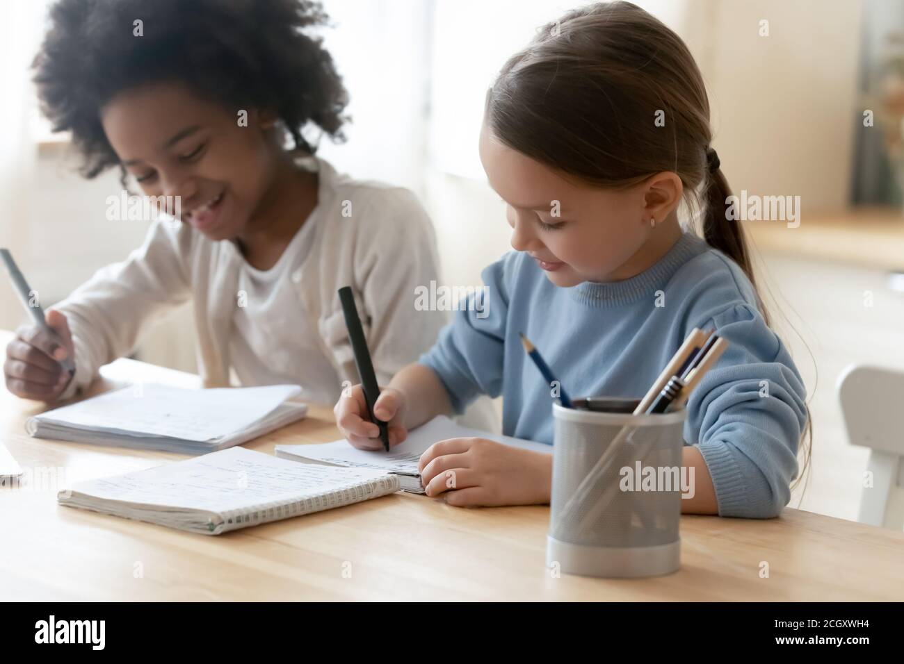 Kleine multirassische Kinder genießen die Vorbereitung Hausaufgaben in Innenräumen. Stockfoto