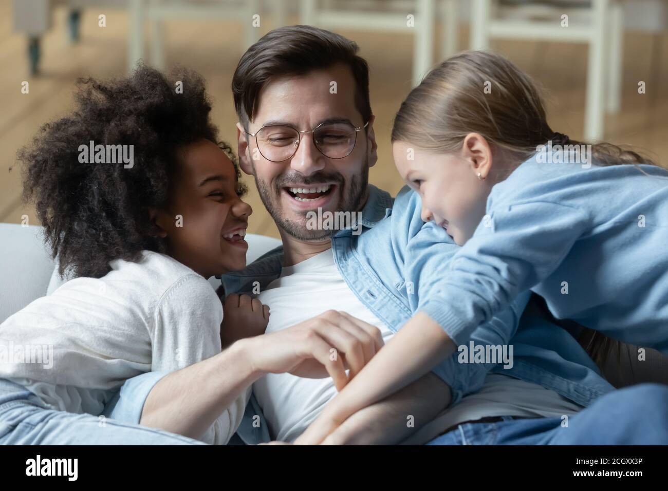 Verspielte kleine Mischlinge kitzeln lachenden jungen Vater. Stockfoto