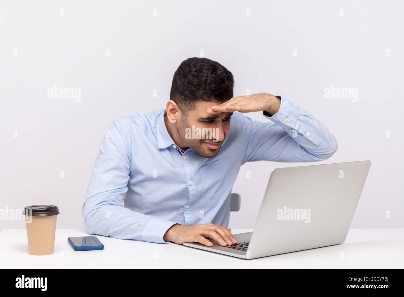 Computer Vision Syndrom. Männlicher Büroangestellter, der am Laptop arbeitet und den Bildschirm sorgfältig betrachtet, die Hand über die Augen hält, die sich auf das Display konzentrieren und e Stockfoto
