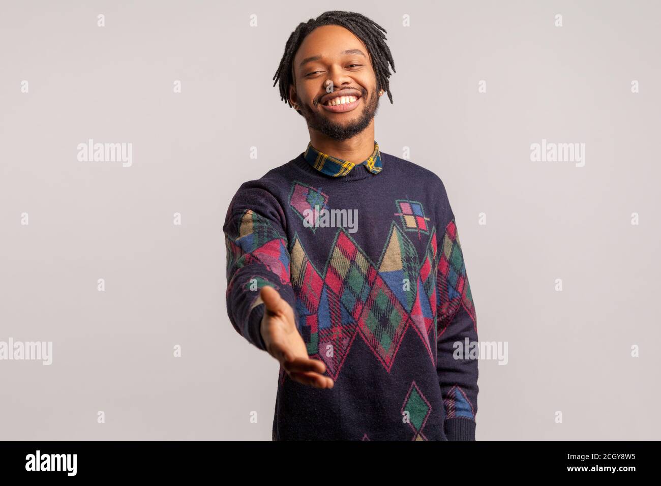 Freundlicher, positiver afrikanischer Mann mit Dreadlocks im trendigen Sweatshirt streut seine Hand mit toothy Lächeln, das sich vorstellt, Freut mich, Sie kennenzulernen. Innen Stockfoto