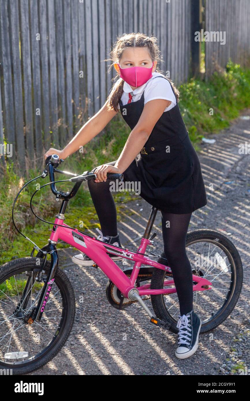 Eine zehnjährige Schülerin in Schuluniform sitzt auf ihrem rosa Fahrrad und trägt eine rosa Gesichtsmaske. Stockfoto
