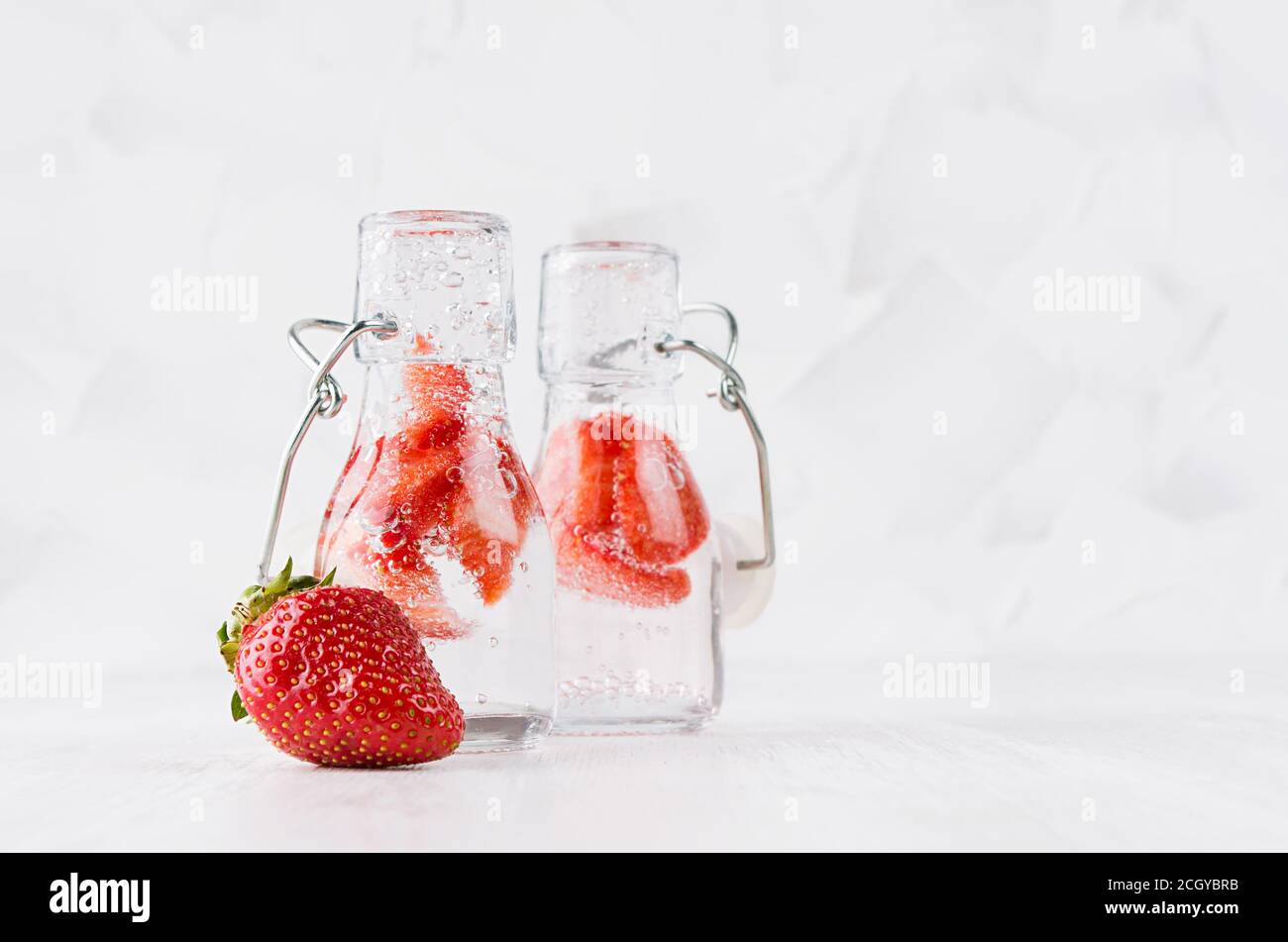 Sommer selbstgemachte Getränke - infundiertes Erdbeerwasser mit geschnittener Beere, Soda in Joch-Flaschen in weichem hellweißem Innenraum, Kopierraum. Stockfoto