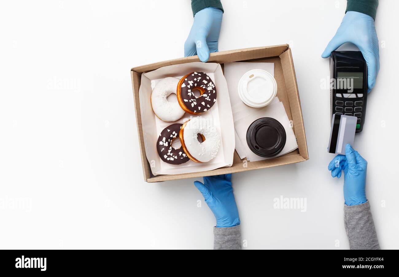 Schnell und Junk-Food. Der Kunde in Gummihandschuhen bezahlt die Bestellung mit Kreditkarte am kontaktlosen Terminal mit leerem Bildschirm und nimmt Donuts und Kaffee Stockfoto