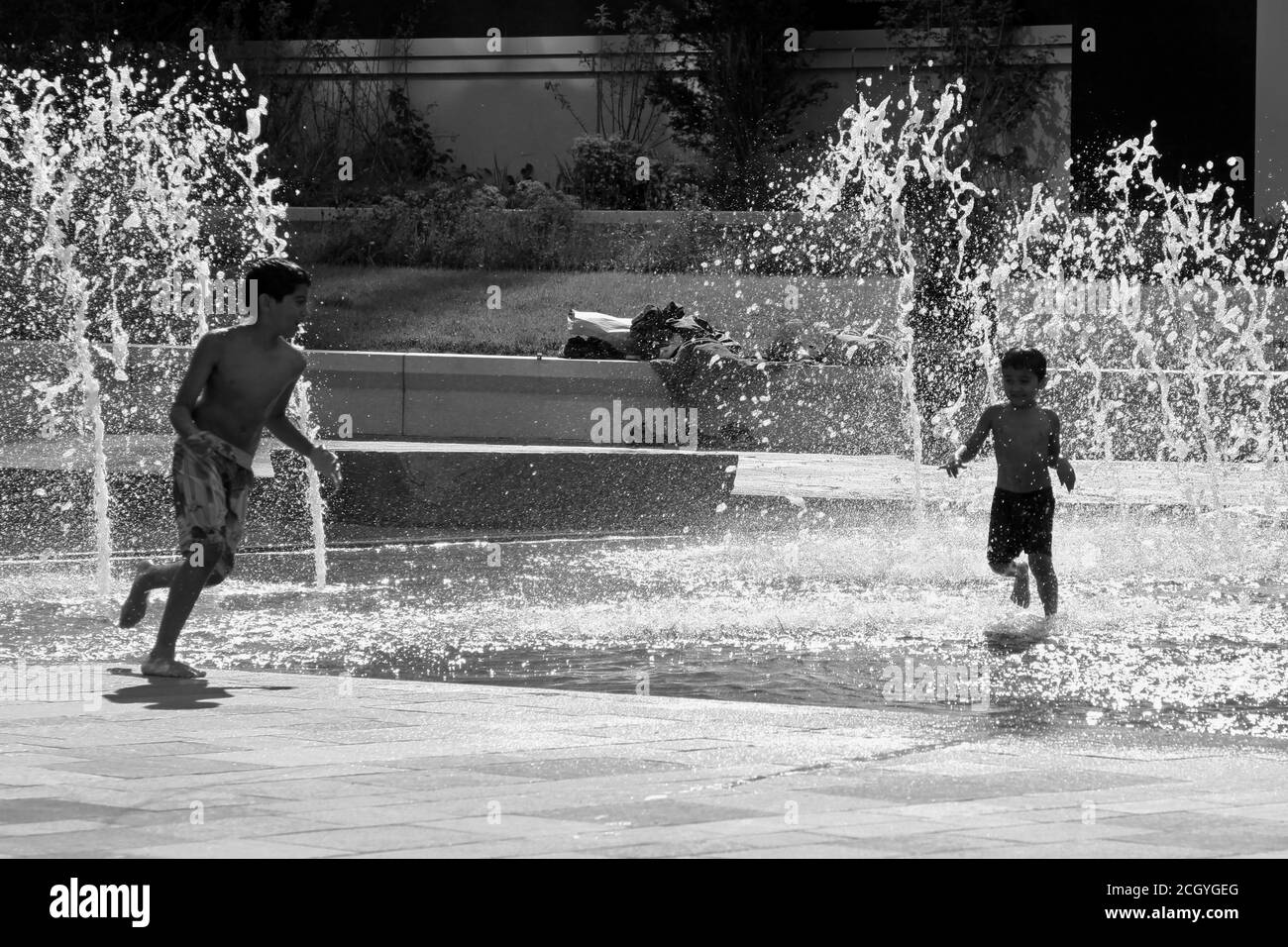 Zwei Jungen jagen einander in Springbrunnen in hell Sonnenschein Stockfoto