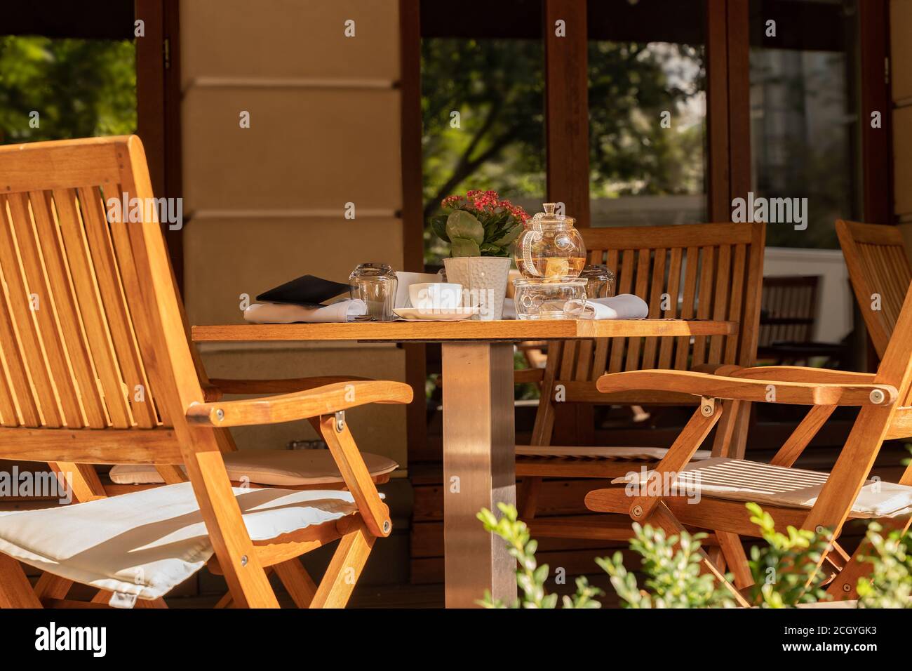 Leere Stühle und Teegeschirr auf dem Tisch eines offenen Cafés oder Restaurants an einem sonnigen Sommertag. Stockfoto