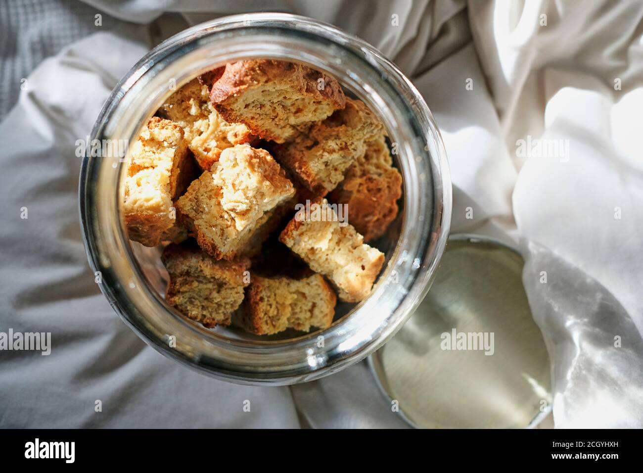 Frisch gebackener Zwieback in einem Glasbehälter auf Bettwäsche und weißer Bettwäsche. Stockfoto