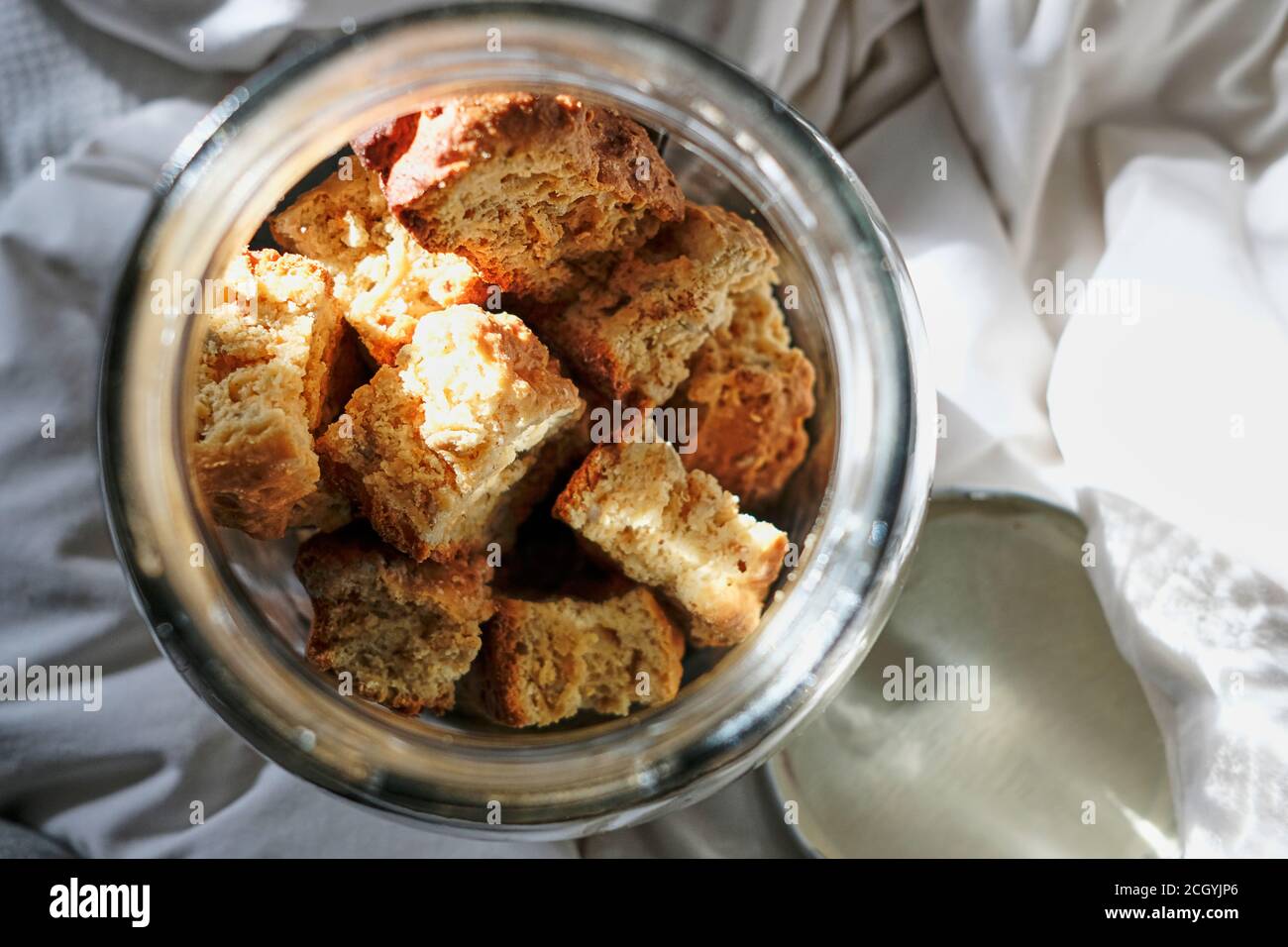 Frisch gebackener Zwieback in einem Glasbehälter auf Bettwäsche und weißer Bettwäsche. Stockfoto