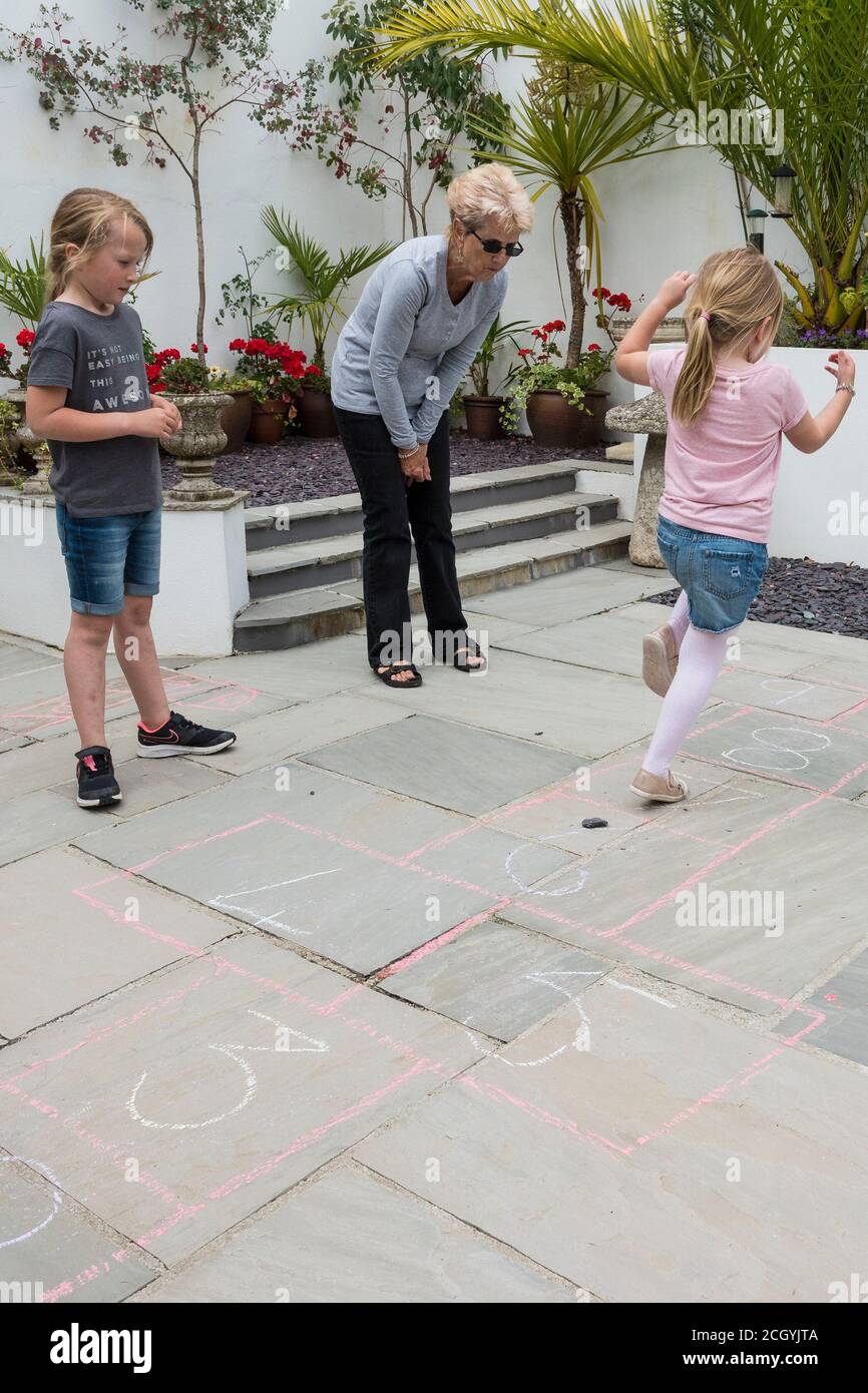 Eine Großmutter lehrt ihre Enkelinnen th traditionelle Spiel von hopscotch. Stockfoto