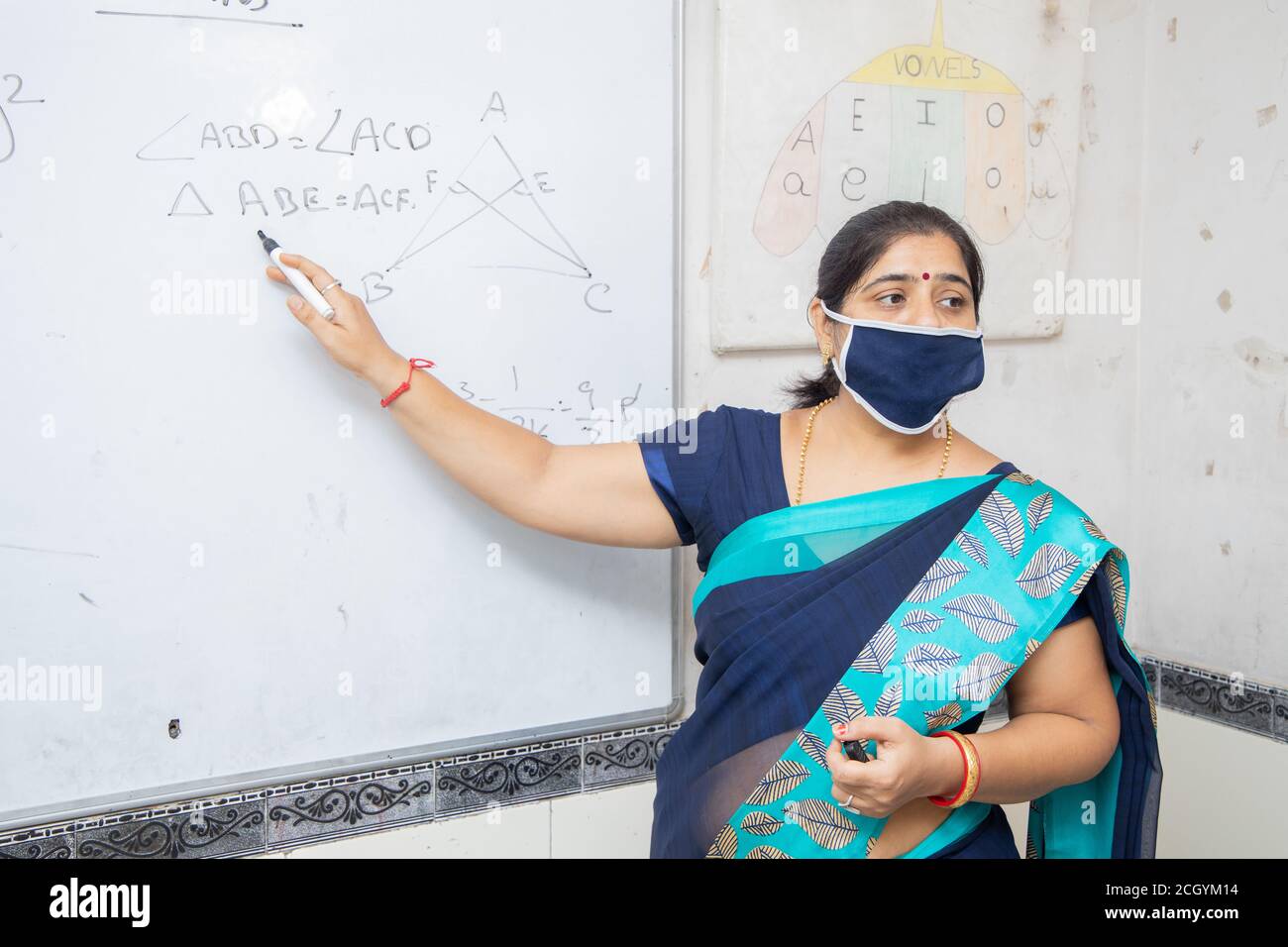 Weibliche Lehrerin Tragen Maske und lehren zeigen auf Whiteboard im Klassenzimmer, indische Schulklasse während covid19 Pandemie, neue Normalität Stockfoto
