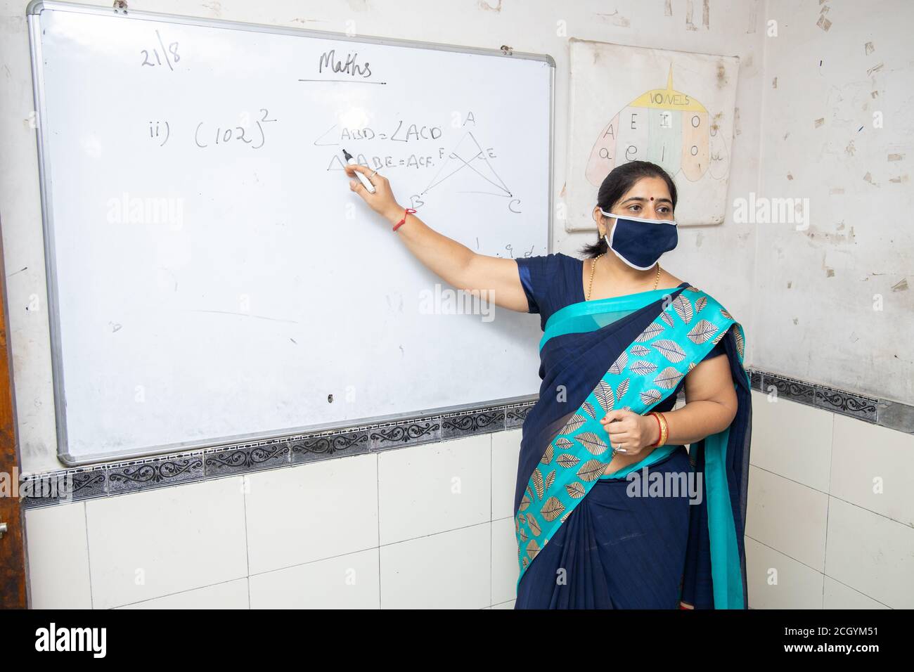 Weibliche Lehrerin Tragen Maske und Saree lehren Mathematik auf Whiteboard im Klassenzimmer, indische Schulklasse während covid19 Pandemie, neue Normalität Stockfoto