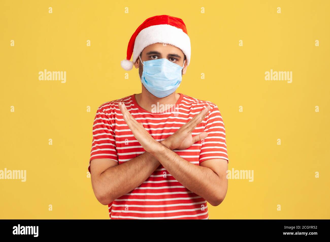 Erschrocken Mann in santa claus Hut mit chirurgischen medizinischen Maske auf Gesicht stehend Kreuzung Hände, zeigt x Zeichen Bedeutung Stopp, Abstand halten. Studio-Zimmer im Innenbereich Stockfoto