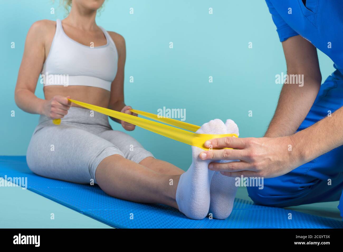 Mädchen führt Übungen mit einem Physiotherapeuten. Cyanfarbener Hintergrund Stockfoto