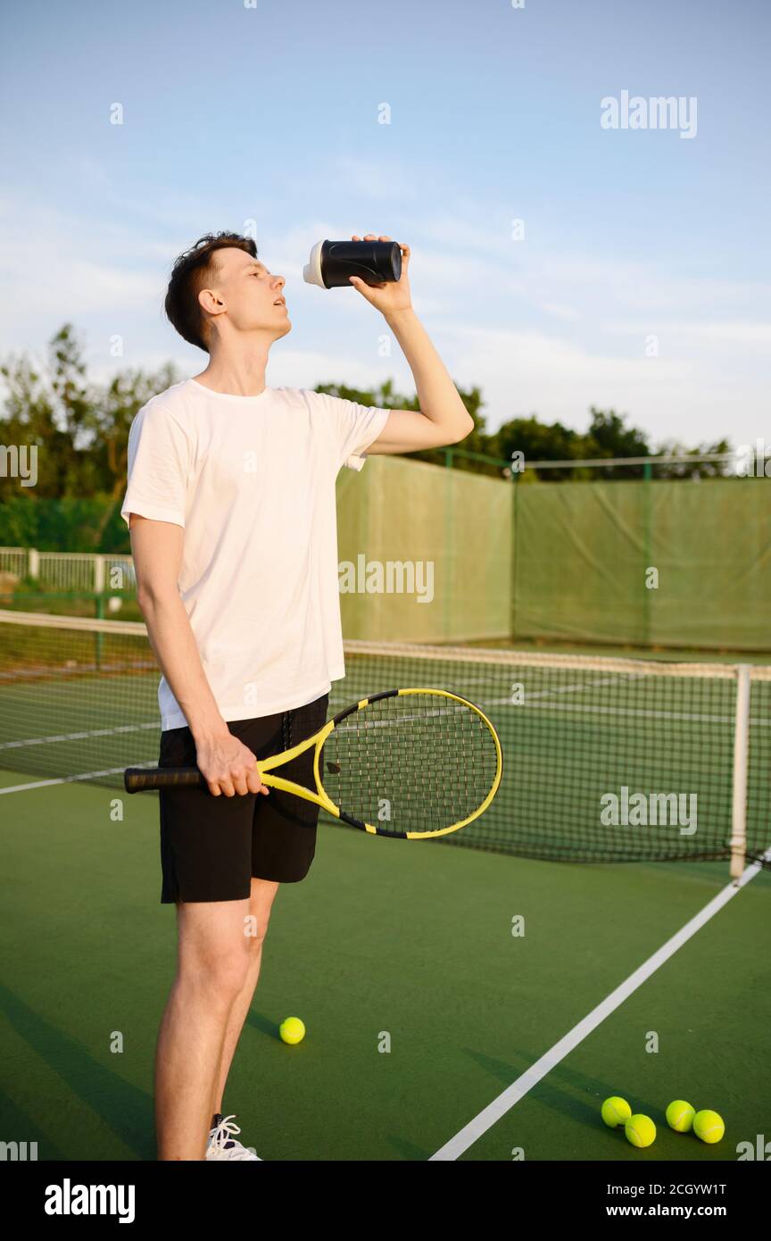 Müder männlicher Tennisspieler trinkt Wasser Stockfoto