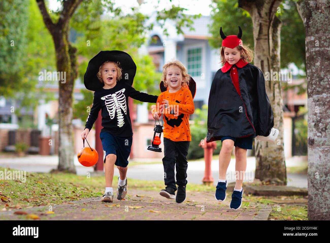 Kind in Halloween-Kostüm. Kinder tricksen oder gönnen sich auf der Vorstadtstraße. Kleiner Junge und Mädchen mit Kürbislaterne und Süßwareneimer. Baby in Hexenhut. Autu Stockfoto