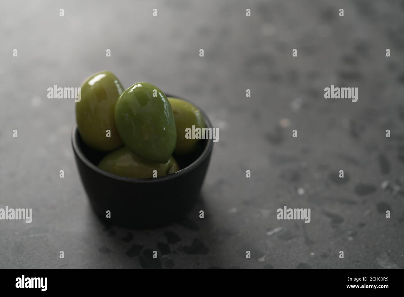 Große grüne Oliven in schwarzer Schale auf Beton Hintergrund, flacher Fokus Stockfoto