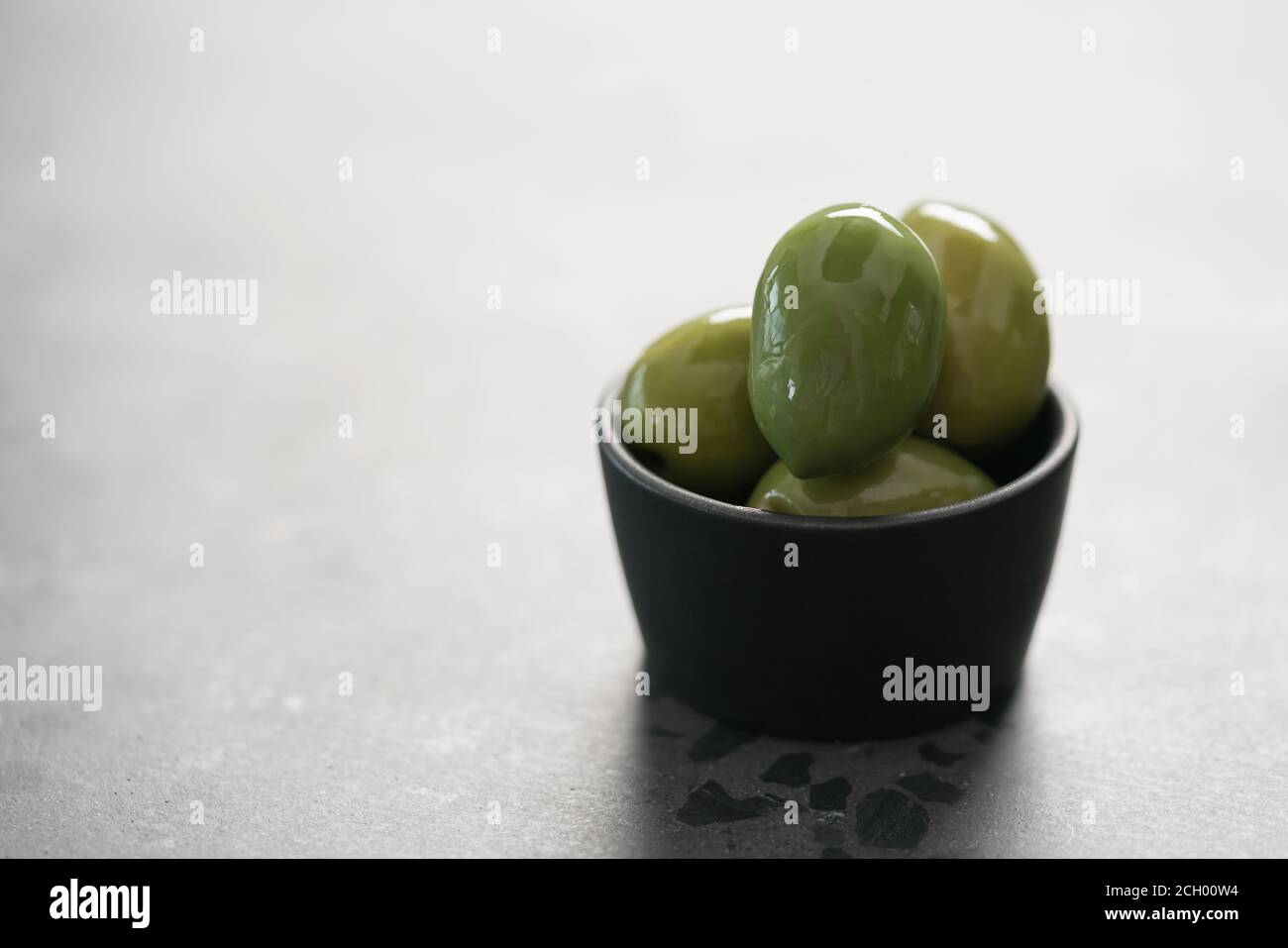 Große grüne Oliven in schwarzer Schale auf Beton Hintergrund, flacher Fokus Stockfoto