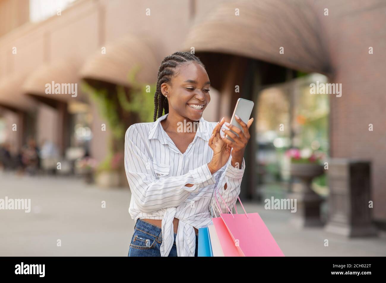 Porträt der Frau hält Pakete und Smartphone, schockiert von Online-Mode-Shop Stockfoto
