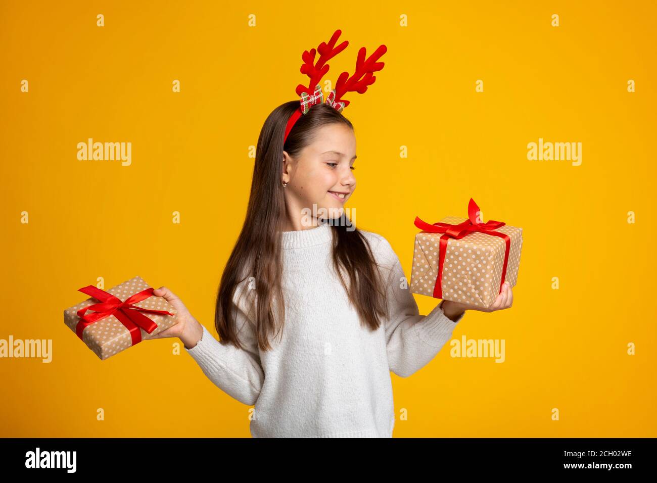 Träume werden an Weihnachten wahr. Lächelndes Mädchen mit Hörnern in Pullover hält Geschenke Stockfoto