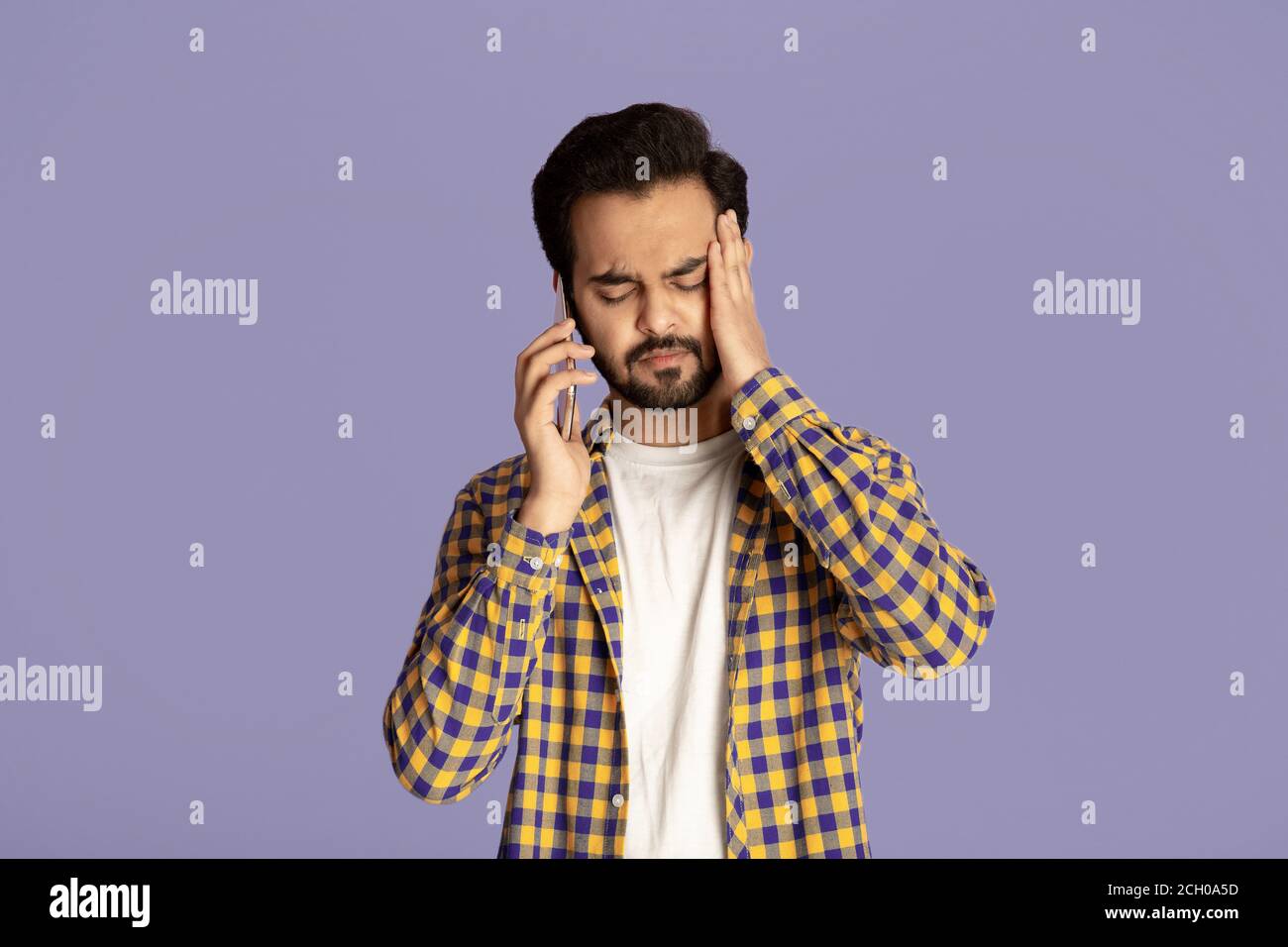 Junger Inder mit Kopfschmerzen oder Depressionen auf dem Smartphone sprechen Über fliedem Hintergrund Stockfoto