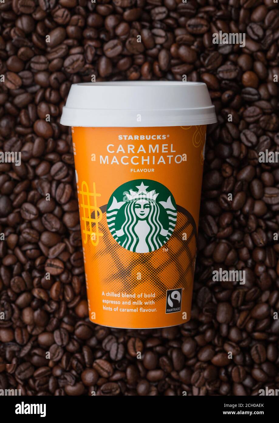 LONDON, UK - September 09, 2020: Papiertasse von Starbucks Caramel Macciato eisgekühlten Kaffee auf der Oberseite der frischen rohen Kaffeebohnen. Stockfoto