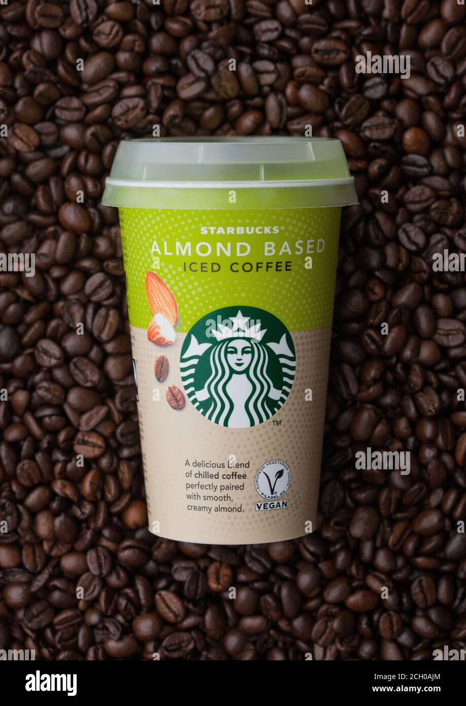 LONDON, UK - September 09, 2020: Papiertasse von Starbucks Almond basiert eiskalten Kaffee auf der Oberseite der frischen rohen Kaffeebohnen. Stockfoto