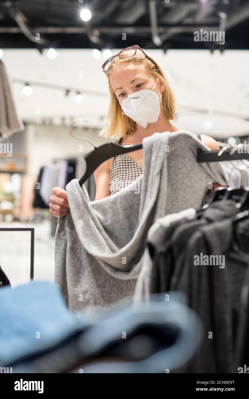 Modische Frau trägt schützende Gesichtsmaske Shopping-Kleidung in Wiedereröffnung Einzelhandelsgeschäft. Neuer normaler Lebensstil während der Corona-Virus-Pandemie Stockfoto