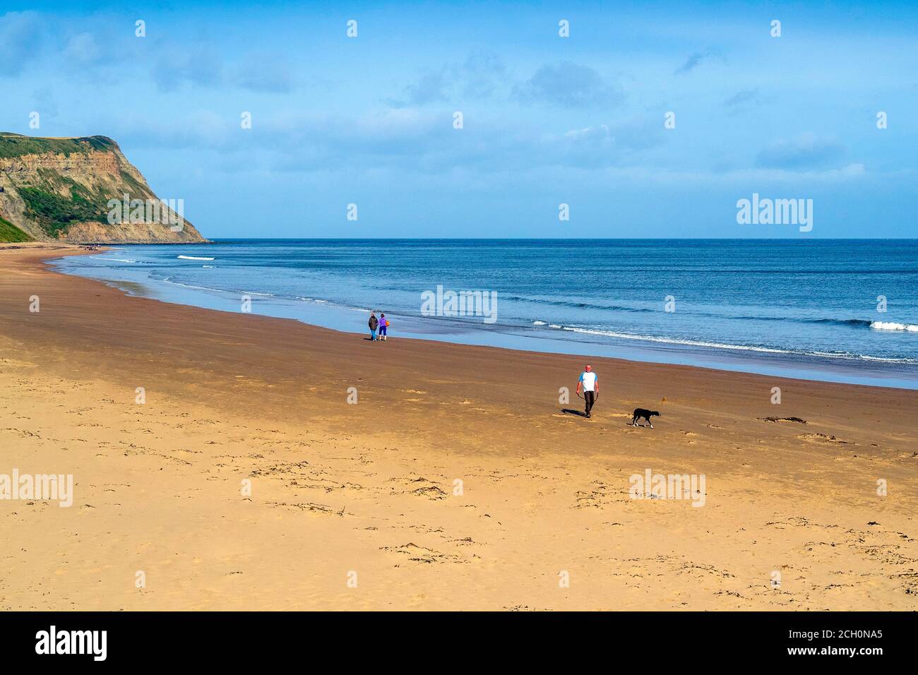 Ein paar Schritte am Cattersty Sands Beach in Skinningrove Cleveland entlang Großbritannien und ein Mann geht mit seinem Hund Stockfoto