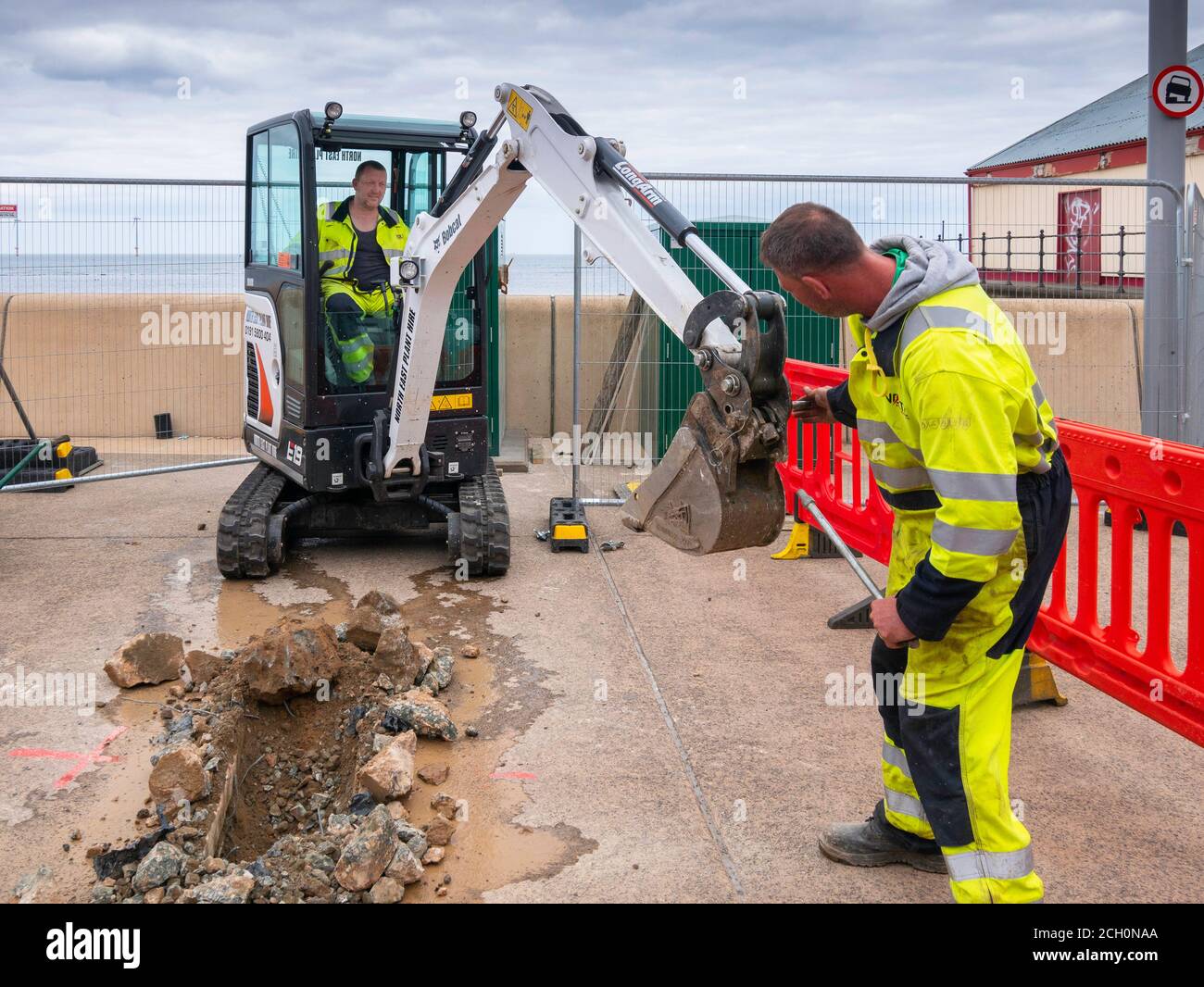 Arbeiter mit Bob Cat Bagger Bagger Aushub einer Kabelgraben Anschluss an einen Schaltschrank am Meer Wand in Redcar Stockfoto