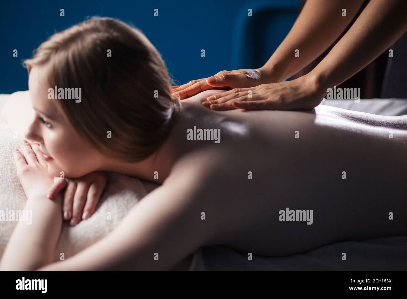 Schöne Frau bekommt Massage im Spa. Hände massieren den Rücken, liegen auf dem Bauch einer Frau Stockfoto