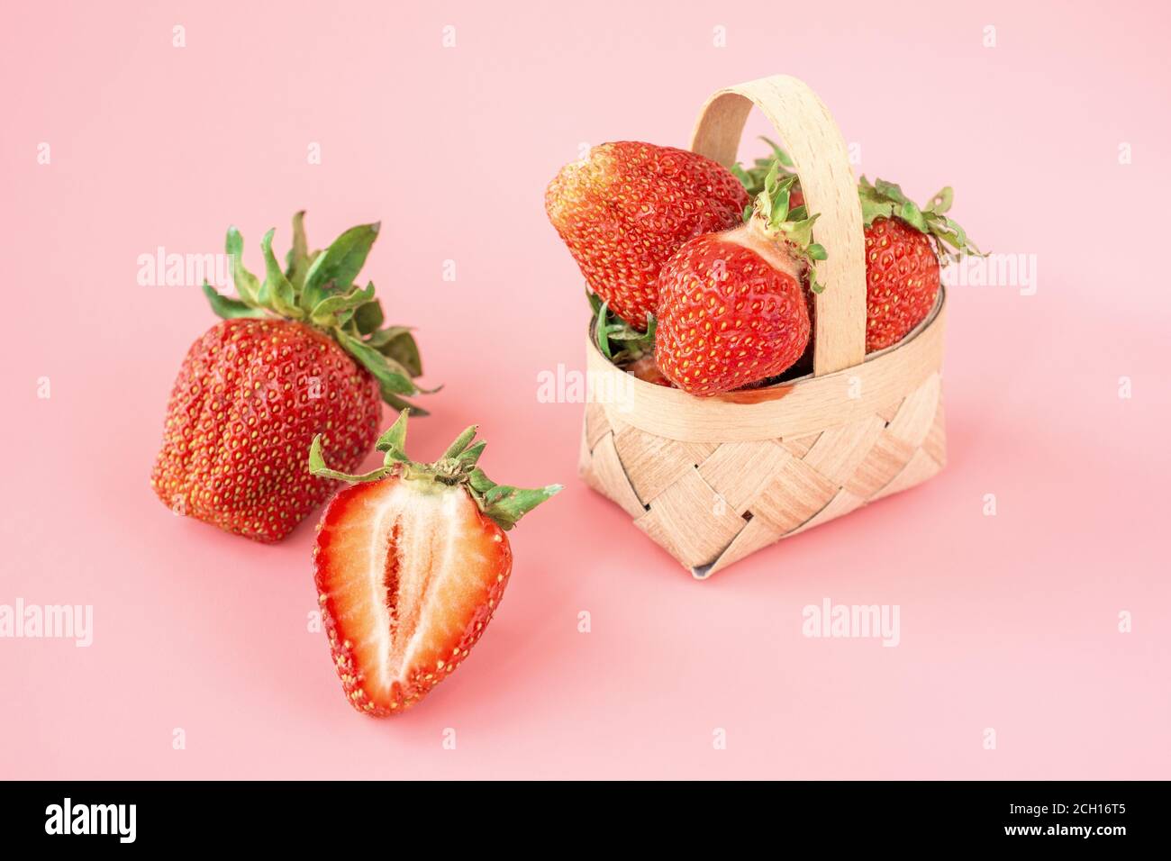 Frische Erdbeeren im Korb, Obst auf Bauernmarkttisch. Frische rote Erdbeeren. Hoch gestapelt und einen kleinen gewebten Korb auf einem rosa Rücken füllen Stockfoto