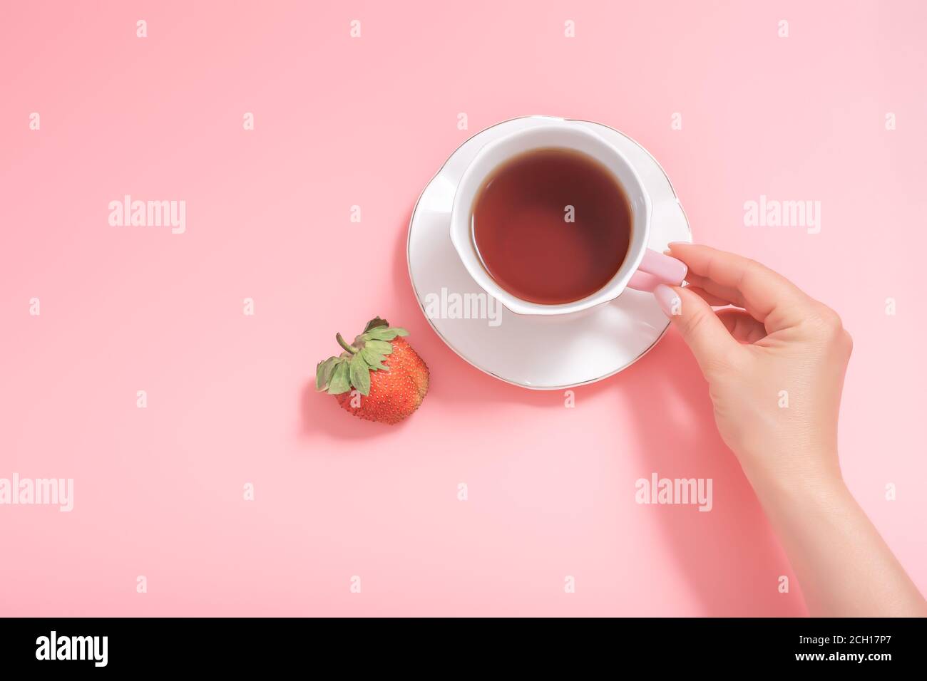 Frauenhand mit einer Tasse Tee und einer Erdbeere auf einem rosa Hintergrund. Draufsicht. Copyspace Stockfoto