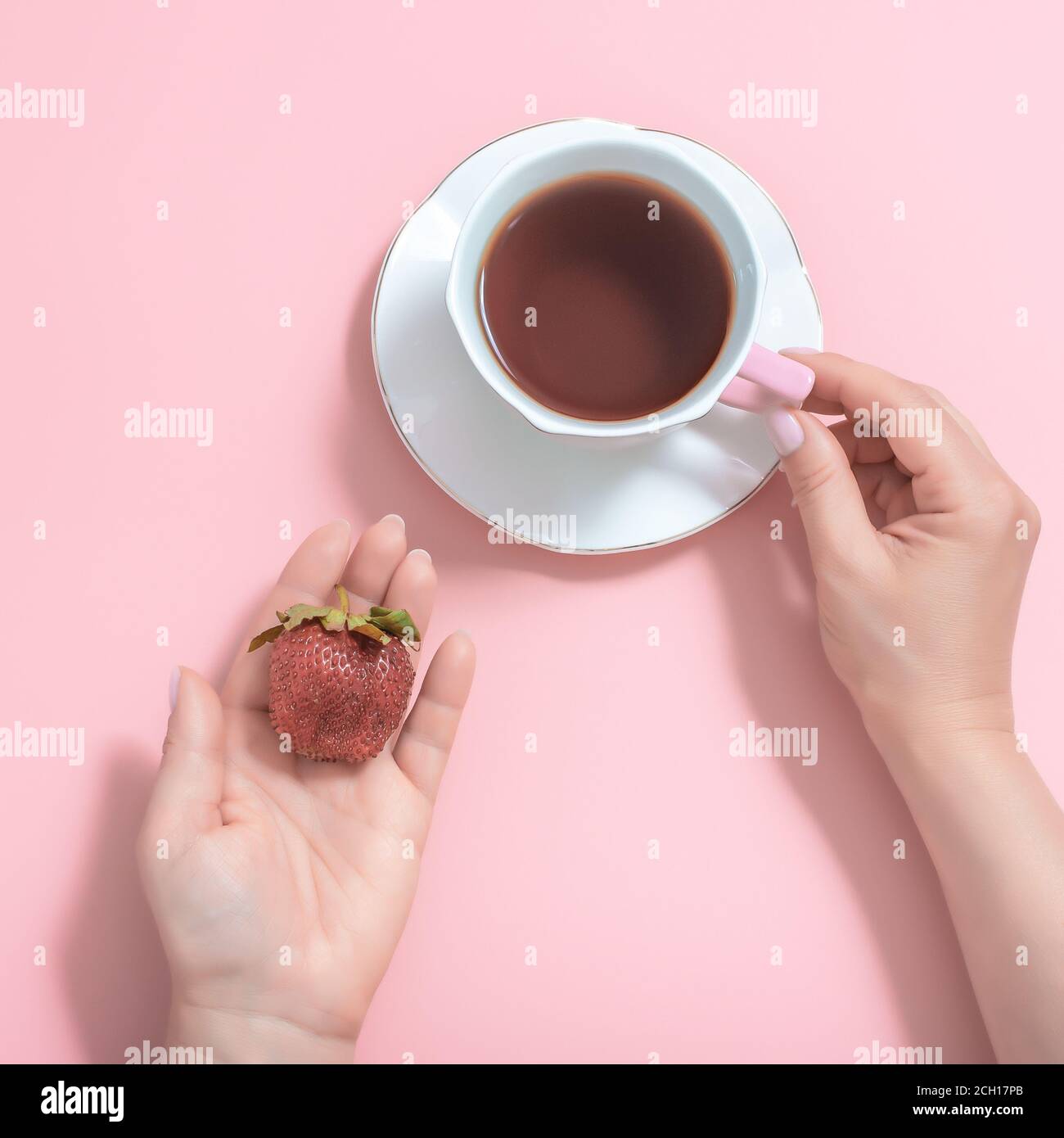 Damenhände mit einer Tasse Tee und Erdbeeren auf einem rosa Hintergrund. Weiße Tasse Tee auf einer weißen Untertasse. Draufsicht Stockfoto