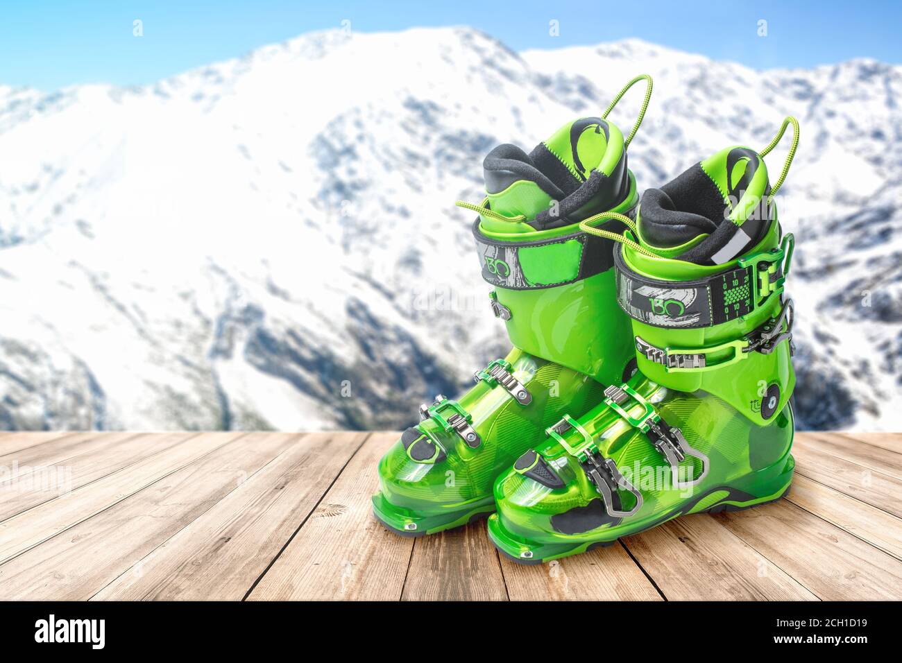 Skischuhe auf einem Holztisch vor dem Hintergrund der Berge. Leuchtend grüne Sport-Skischuhe Stockfoto