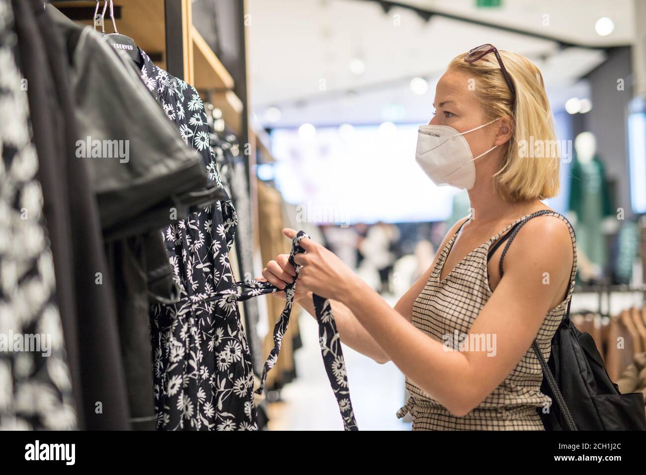 Modische Frau trägt schützende Gesichtsmaske Shopping-Kleidung in Wiedereröffnung Einzelhandelsgeschäft. Neuer normaler Lebensstil während der Corona-Virus-Pandemie Stockfoto