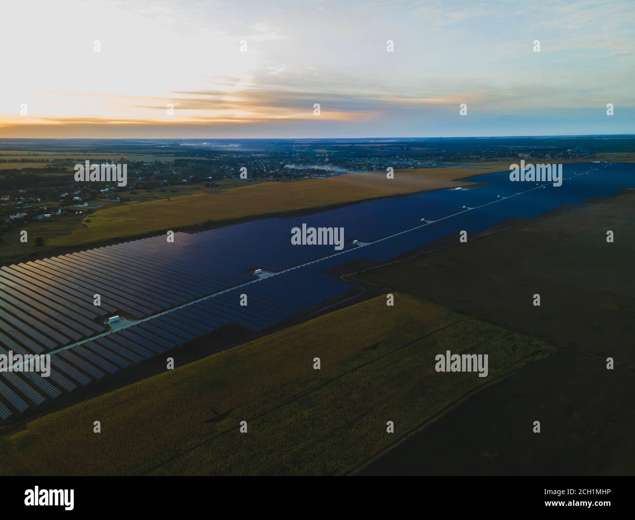 Luftdrohne Blick in große Sonnenkollektoren auf einer Solarfarm in großem Feld auf dem Land bei hellem Sonnenuntergang. Solarzellen Kraftwerke, bunte Foto Stockfoto