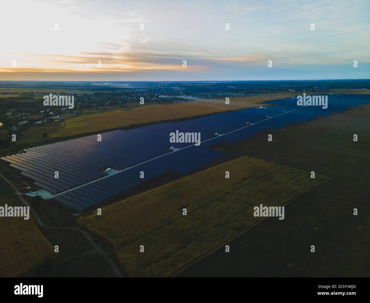 Luftdrohne Blick in große Sonnenkollektoren auf einer Solarfarm in großem Feld auf dem Land bei hellem Sonnenuntergang. Solarzellen Kraftwerke, bunte Foto Stockfoto