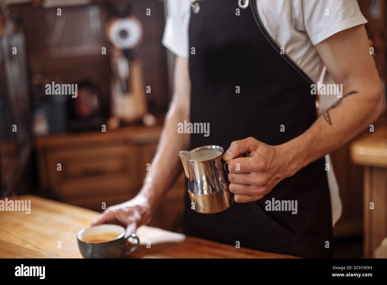 Nahaufnahme beschnittene Seitenansicht des Mannes, der Milch gießt Und bereiten Sie frischen Cappuccino zu Stockfoto