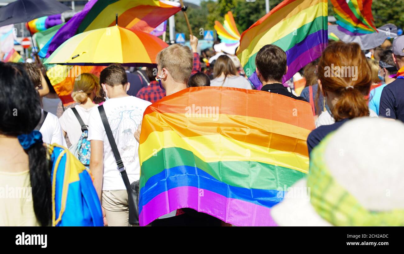 gleichstellungsmarsch der LGBT. Zwei Schwule halten die Hände und gehen stolz Parade. Junge Menschen in Regenbogenkleidung und Symbolen kämpfen für LGBTQ+-Rechte. Stockfoto