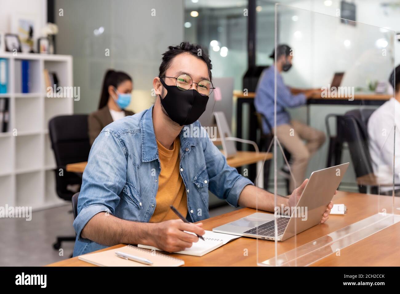 Portrait des asiatischen Büro Mitarbeiter Geschäftsmann tragen Schutzmaske Gesicht Arbeiten Sie in einem neuen normalen Büro mit interracial Kollegen im Hintergrund Als soziale d Stockfoto
