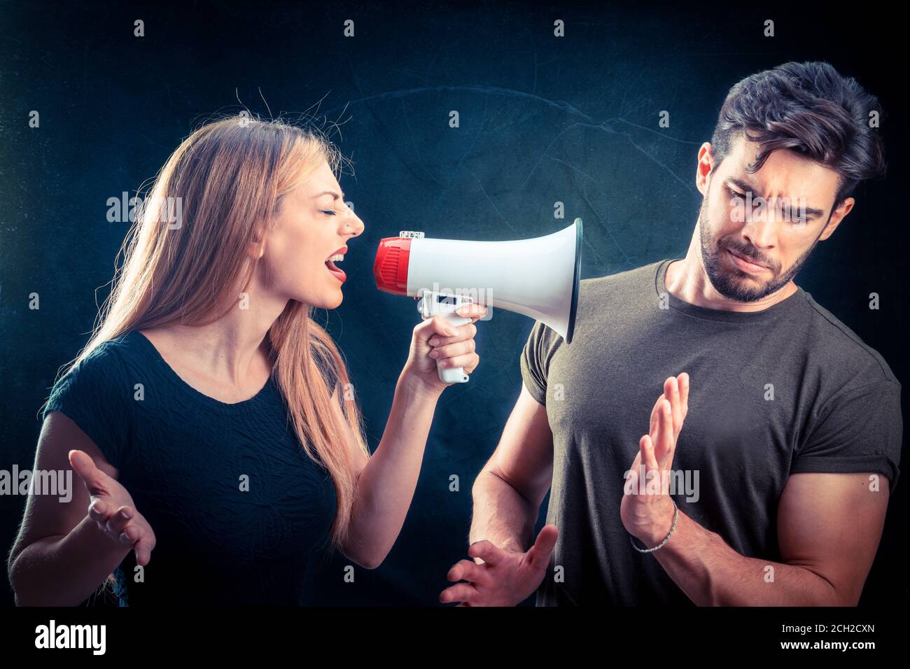 Eine zornige hysterische Frau, die gegen einen Jungen lautes Megaphon schreit Dunkler Wandhintergrund Stockfoto