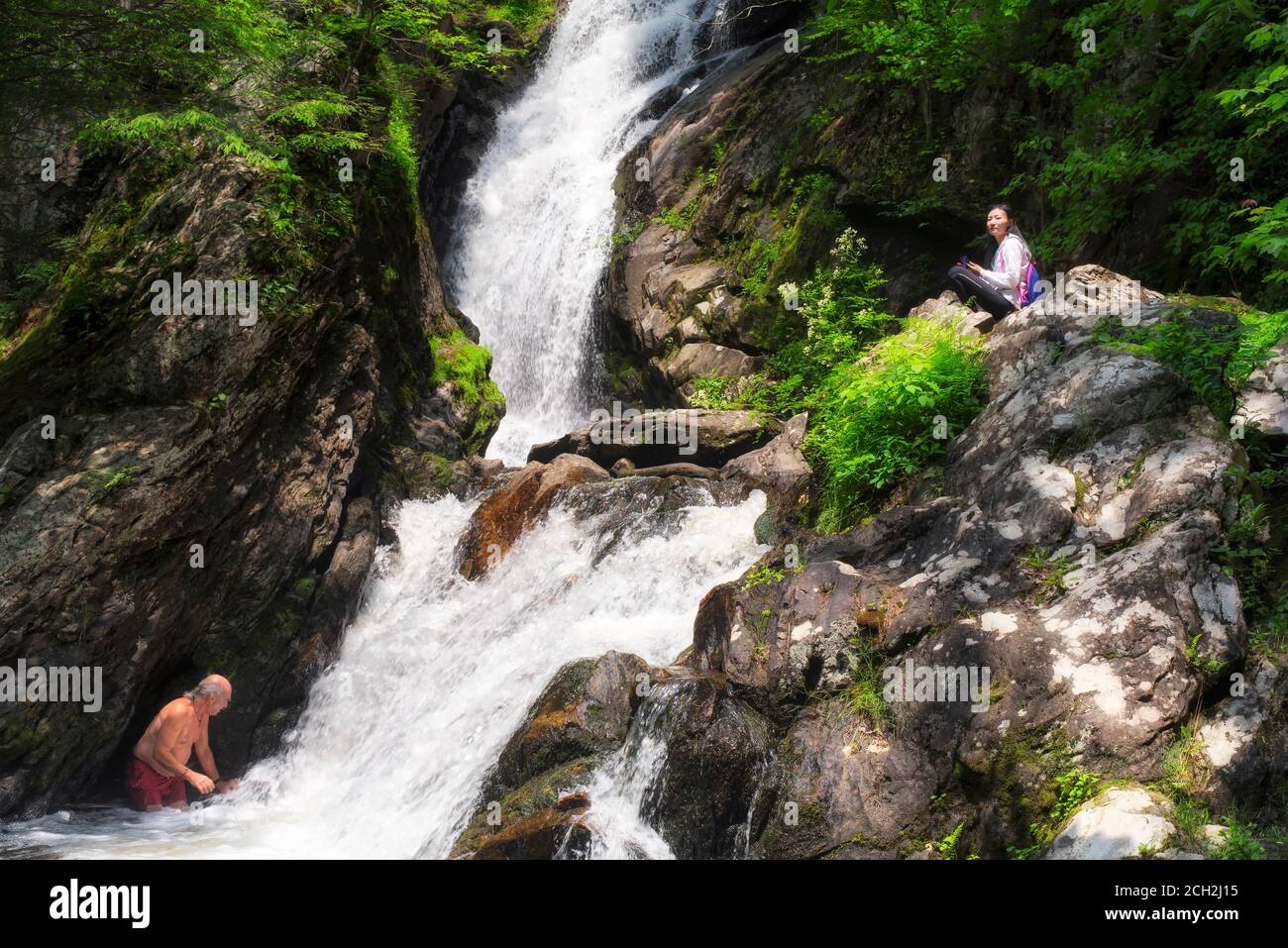 Ein Mann schwimmt am Fuße der Campbell Falls, während eine chinesische Frau an einem Sommertag in den berkshires im Westen von Massachusetts sitzt und zuschaut. Stockfoto