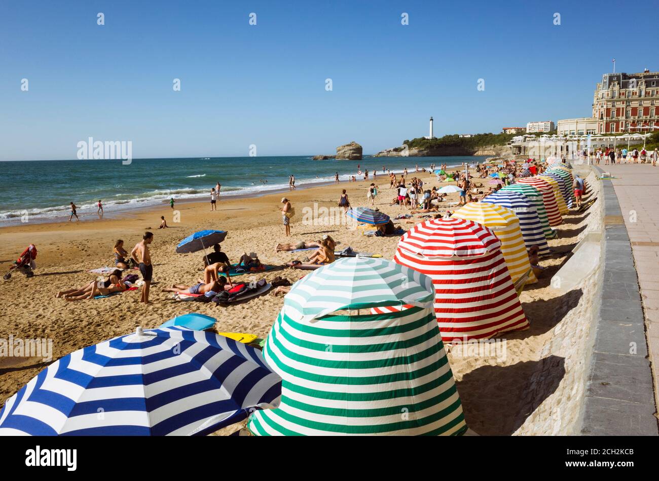 Biarritz, Französisch Baskenland, Frankreich - 19. Juli 2019 : Strandgänger unter bunten Sonnenschirmen am La Grande Plage, dem größten Strand der Stadt. Hôtel d Stockfoto