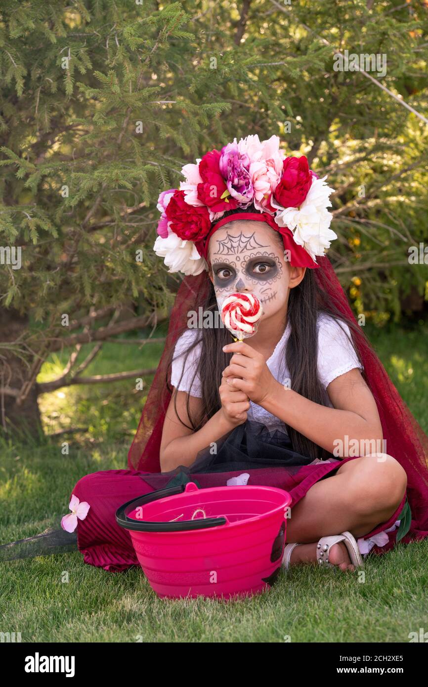 Nettes Mädchen mit Farbe auf Gesicht und große Lollypop in Hände sitzen auf grünem Gras Stockfoto