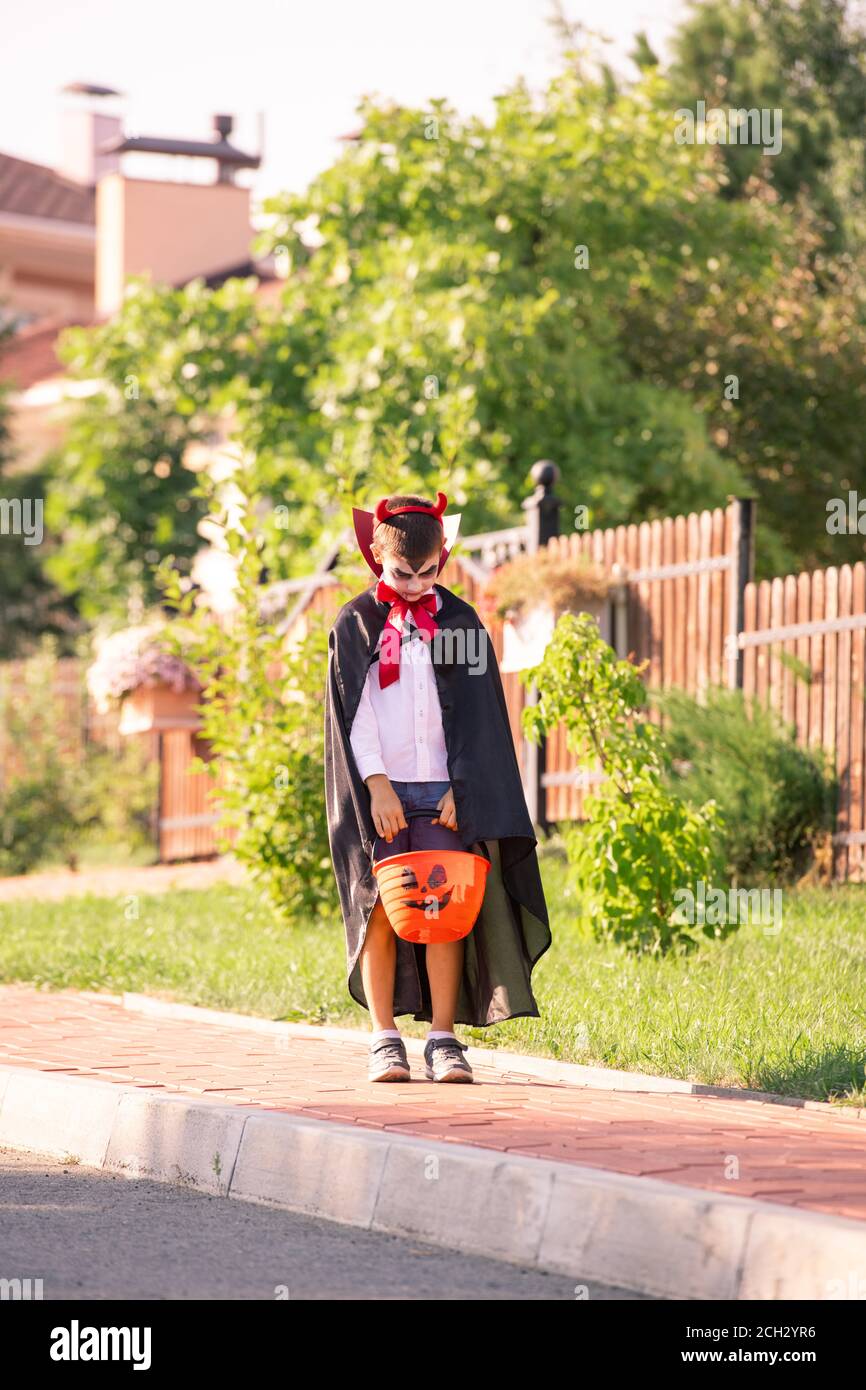 Kleiner Junge im Kostüm von halloween Teufel mit Korb von Leckereien stehen auf der Straße Stockfoto