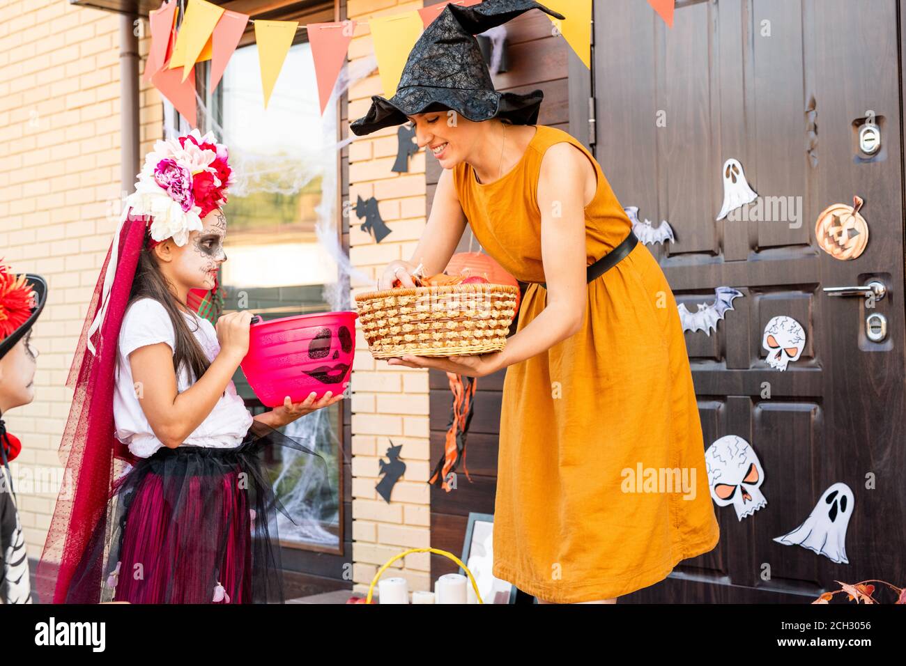 Junge Frau in gelbem Kleid und schwarz Hexenhut biegen Von niedlichen halloween-Mädchen Stockfoto