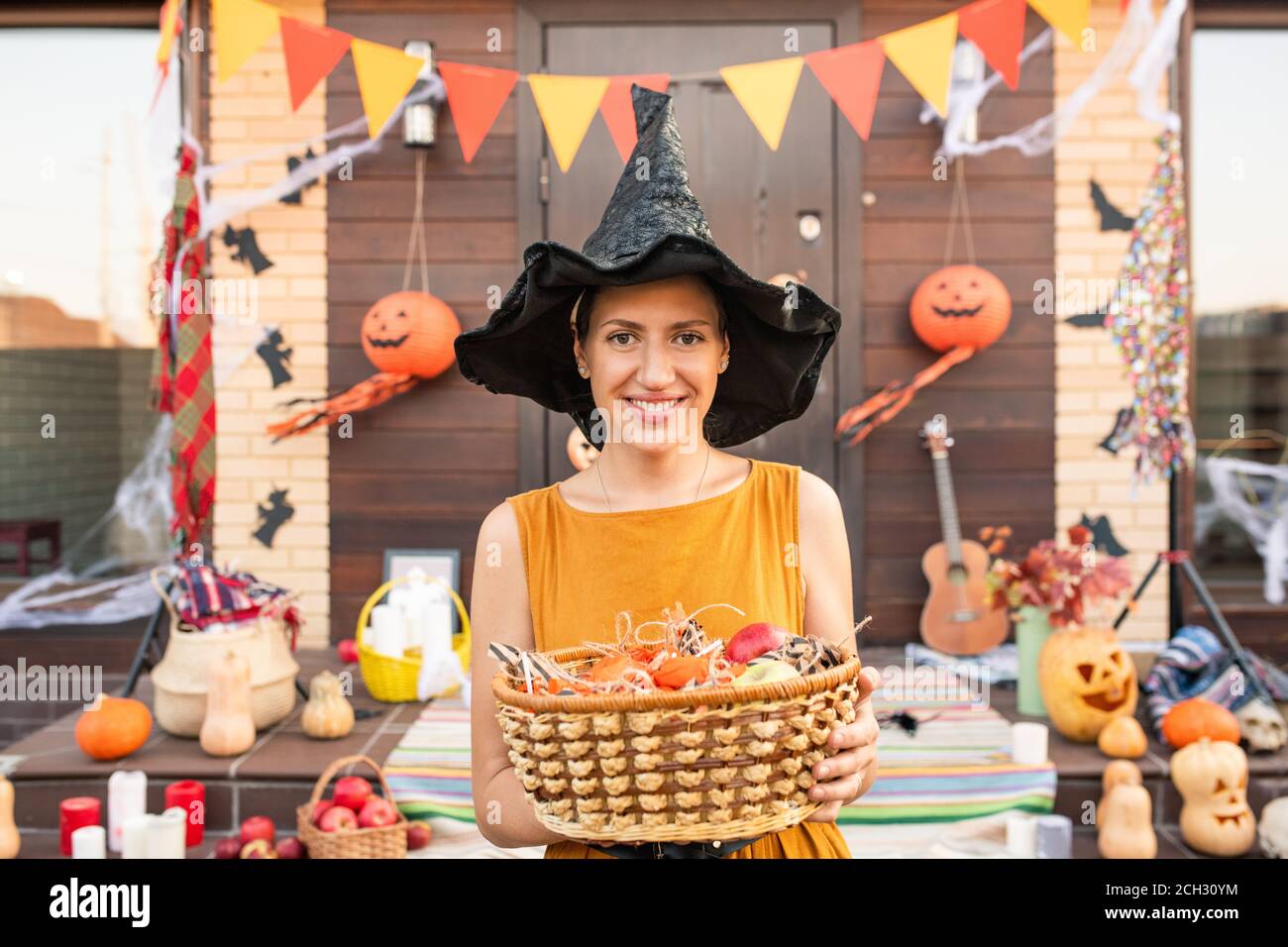 Junge hübsche Frau in schwarzem Hut von halloween Hexe halten Korb mit Süßigkeiten Stockfoto